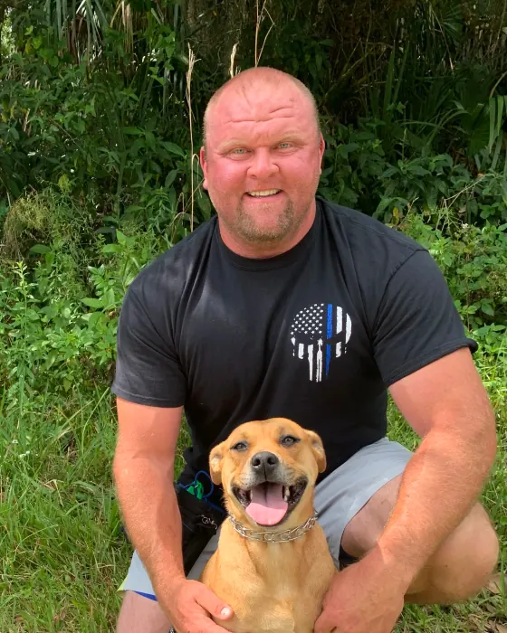 Chad Walker crouching in a grassy Florida yard, smiling, with a tan dog sitting between his knees
