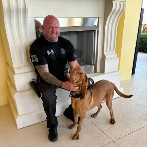 Chad Walker in a police K-9 shirt kneeling beside a young bloodhound indoors