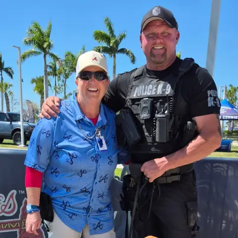 Chad Walker in his Police K-9 vest standing with a visitor and a bloodhound at an outdoor community event