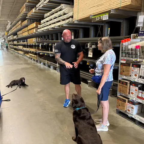 Chad Walker working two dogs on leash down a home improvement store aisle while a third holds a down-stay