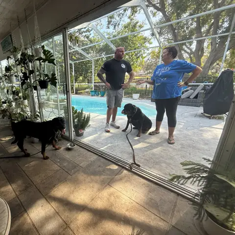 A trainer and an owner working a dog beside the pool while a second waits on the lanai