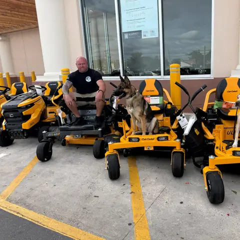 Chad Walker and three dogs holding position on a row of zero-turn mowers outside a dealership