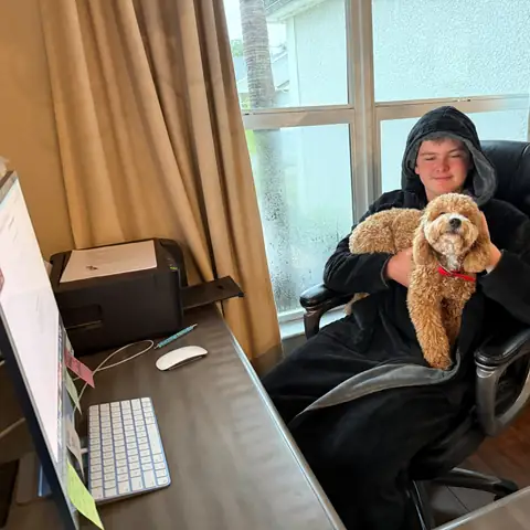 A young handler holding an apricot goldendoodle in an office chair