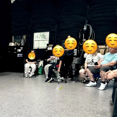 A group obedience class indoors with dogs holding place on raised cots, the owners’ faces covered by emoji stickers