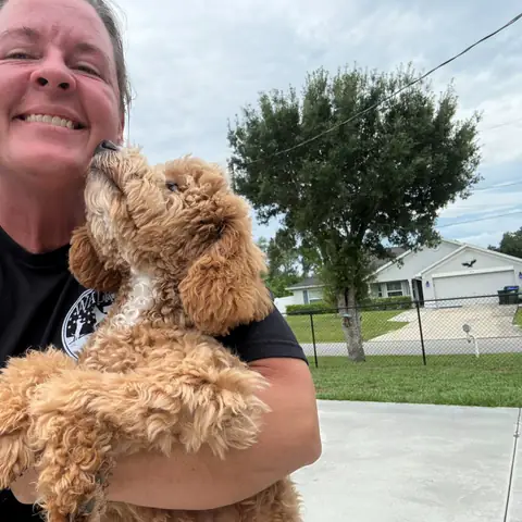Kelly Walker holding an apricot doodle outside the training yard