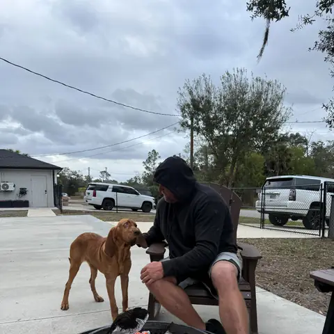 A tan dog greeting its owner beside a lit fire pit on an overcast afternoon