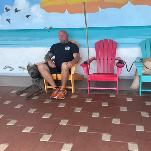 A trainer seated with two dogs among bright Adirondack chairs against a painted beach mural